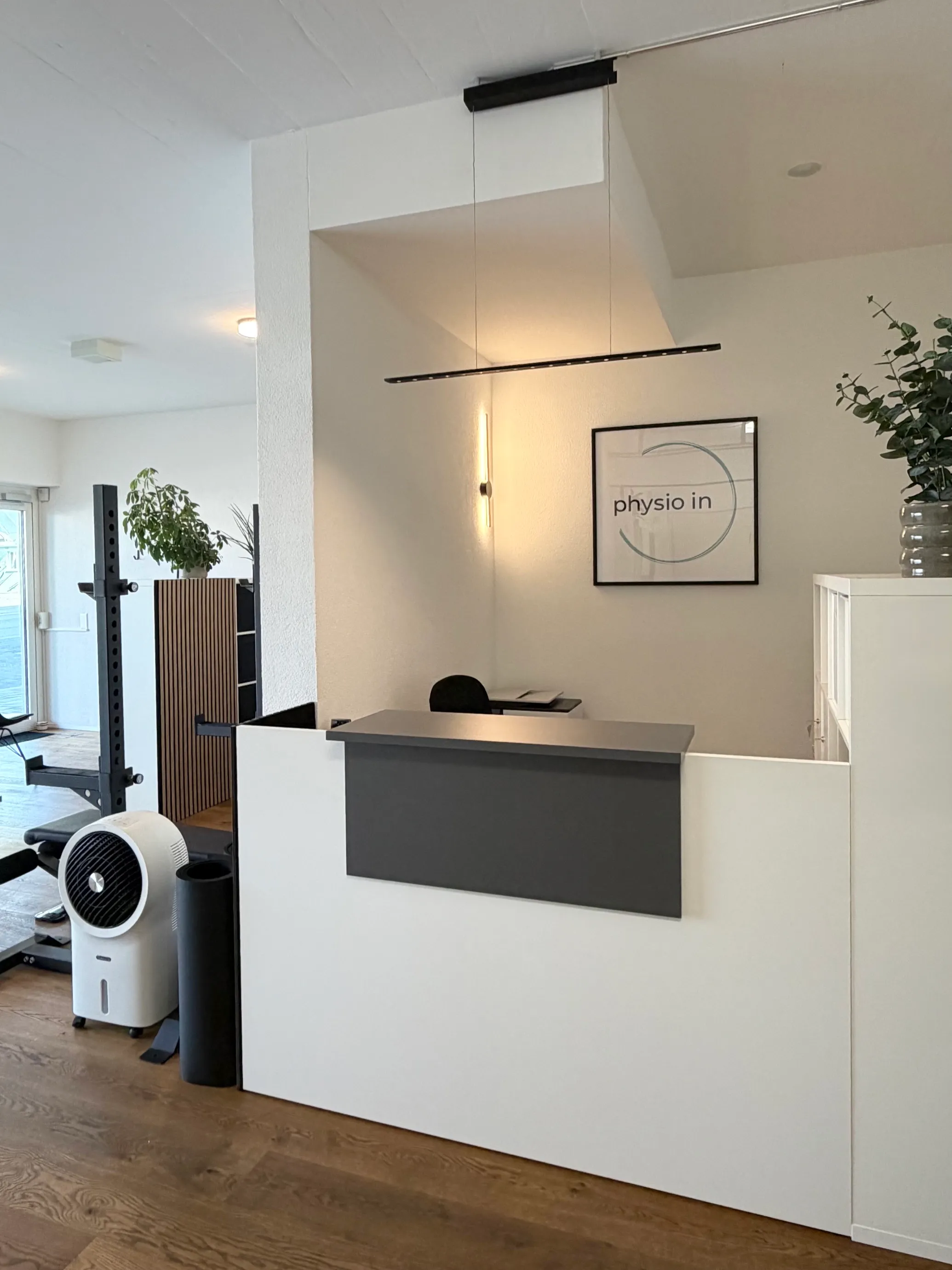 Praxisräumlichkeiten von physio in: Empfangstheke, dahinter das Logo von physio in an der Wand